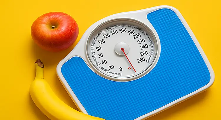 Blue bathroom scale reading 160 lbs on yellow background with a red apple and yellow banana beside it.