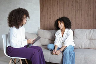 Two women engaged in conversation on a couch, embodying the comfort and support of friendship as a form of therapy.