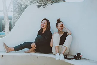 Two friends sit on a wall, hands resting on their knees, embodying the joy and companionship of true friendship.