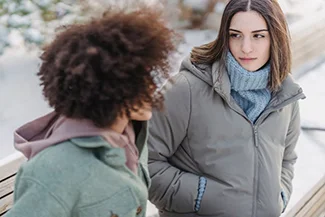 Two women converse on a snowy bench, showcasing the warmth of friendship amidst challenging times.