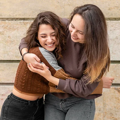 Two young women smile and hug, embodying the essence of friendship and unconditional love, celebrating their close bond.