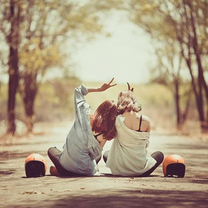 Two women seated on the ground with hands uplifted, symbolizing the rarity and luck of true friendship.