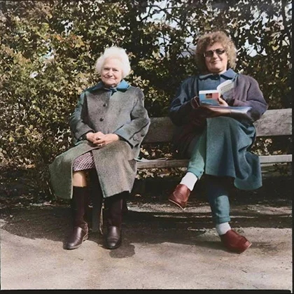 Two older women sit on a bench, sharing books and laughter, embodying the healing power of friendship.