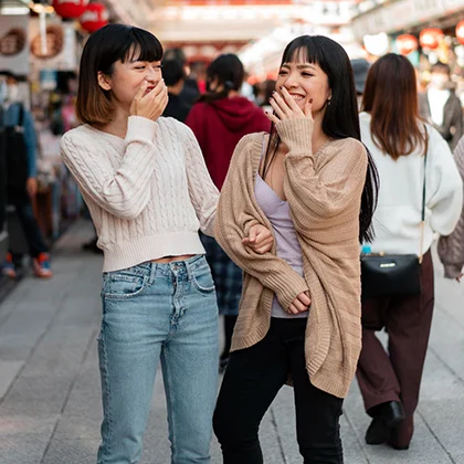 Two women enjoy a moment of laughter on a city street, celebrating the joy and warmth of their friendship.