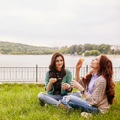 Two women relaxing on the grass, embracing friendship and sharing meaningful moments in a tranquil outdoor space.