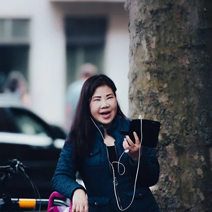 A woman sits on a bench, using a tablet and wearing headphones, embodying the connection of true friendship despite distance.