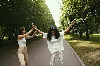 Two women in white attire joyfully dance together in a park, embodying friendship and the spirit of giving.