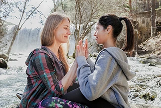 Two women seated on a rock by a river, enjoying each other's company and the calming influence of their friendship.