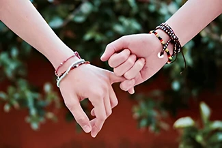 Two friends holding hands, adorned with colorful bracelets, symbolizing love and understanding in their bond.