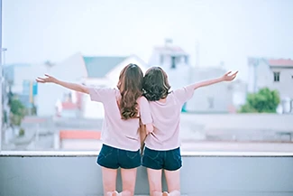 Two young women on a ledge, arms wide open, celebrating their friendship and the joy of chosen family.