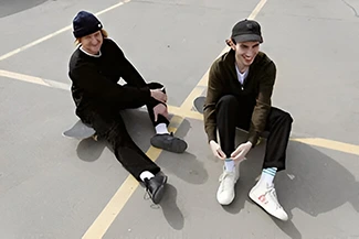 Two young men sit on the ground with skateboards, enjoying friendship and the richness it brings to their lives.