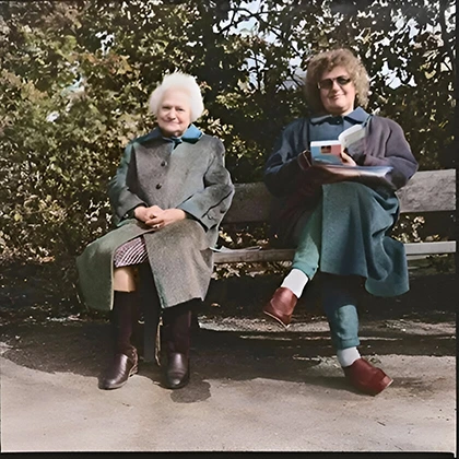 Two older women sit on a bench, sharing books and laughter, embodying the healing power of friendship.