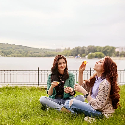 Two women relaxing on the grass, embracing friendship and sharing meaningful moments in a tranquil outdoor space.