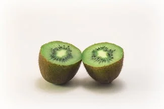 Two halved kiwis displayed on a clean white background, showcasing their vibrant green flesh and tiny black seeds.