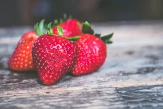 Three ripe strawberries arranged on a rustic wooden table, showcasing their vibrant red color and fresh green leaves.