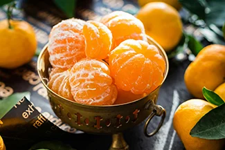 A bowl filled with vibrant tangerine sits elegantly on a wooden table, showcasing a fresh and inviting display of fruit.