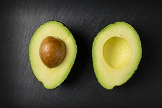 A black surface features two halves of an avocado, highlighting the rich green interior and contrasting with the dark background.