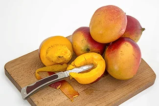 A wooden cutting board displaying ripe mangoes alongside a sharp knife, ready for preparation.