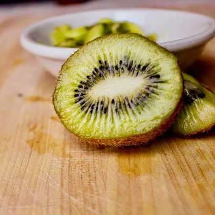 A ripe kiwi fruit positioned on a cutting board, emphasizing its fuzzy exterior and bright green flesh ready for slicing.