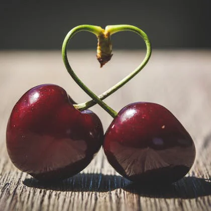 Two cherries with a heart shape resting on a wooden surface, symbolizing love and sweetness in a natural setting.