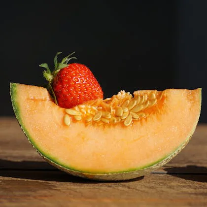 A slice of cantaloupe garnished with a fresh strawberry on top, showcasing vibrant colors and a refreshing summer treat.