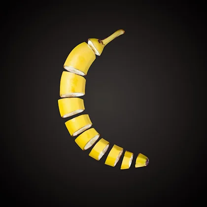 A sliced banana lies on a black background, with its yellow interior contrasting sharply against the dark surface.