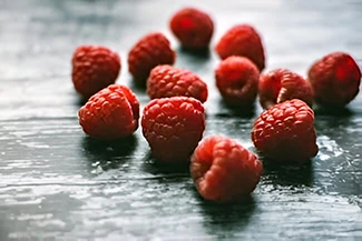 A close-up of fresh raspberries scattered on a rustic wooden table, showcasing their vibrant red color and texture.