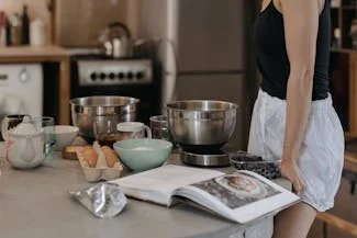 A woman stands in a kitchen, holding a book and a bowl of food, emphasizing the benefits of healthy home cooking.