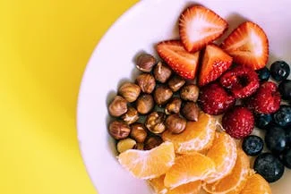 A vibrant bowl filled with assorted fruits and nuts, set against a cheerful yellow background, promoting healthy snacking options.