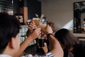 Friends raising their glasses in a toast at a bar, enjoying the moment while considering the health effects of excessive drinking.