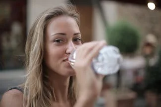 A woman hydrating by drinking water from a bottle, emphasizing the importance of hydration for overall health.