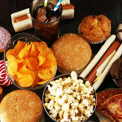 An assortment of processed foods: pizza, hot dogs, soda, popcorn, and candy, highlighting unhealthy fats, sugar, and salt.