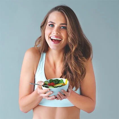 A woman in a sports bra holds a bowl of salad, embodying mindful eating and promoting healthier food choices.