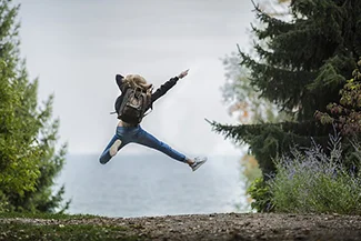 A person leaps joyfully above a lush forest, representing the pursuit of health and happiness in a natural setting.