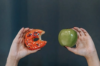 Two hands hold an apple and a donut, symbolizing the choice for healthier eating habits for a better future.