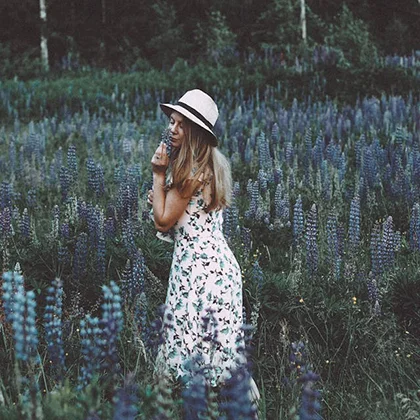 A woman in a stylish hat and dress walks amidst a sea of blue flowers, reflecting serenity and the benefits of proper breathing.