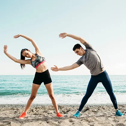 Two people performing yoga on the beach, highlighting the uplifting feelings of peace and well-being through exercise.