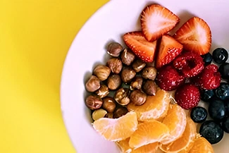A vibrant bowl filled with assorted fruits and nuts, set against a cheerful yellow background, promoting healthy snacking options.