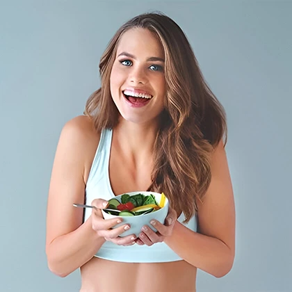 A woman in a sports bra holds a bowl of salad, embodying mindful eating and promoting healthier food choices.