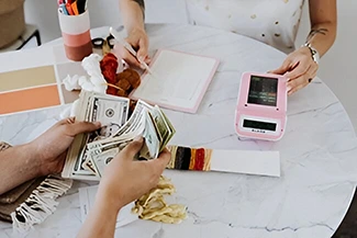 Two people at a table with cash and a pink phone, representing the idea that health is an investment, not an expense.