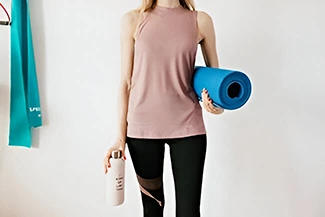 A woman dressed in a pink tank top and black leggings stands with a yoga mat, promoting the importance of daily body care.
