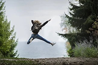 A person leaps joyfully above a lush forest, representing the pursuit of health and happiness in a natural setting.