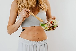 A woman in a white tank top holds a fresh salad, embodying the principle that eating well is a form of self-respect.
