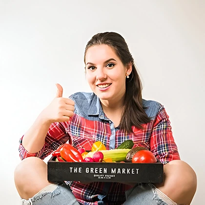 A woman holds a box of fresh vegetables, smiling and giving a thumbs up, promoting healthy food choices for a better future.