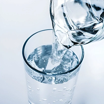 A glass is filled with water being poured, illustrating the necessity of drinking water for proper body function.