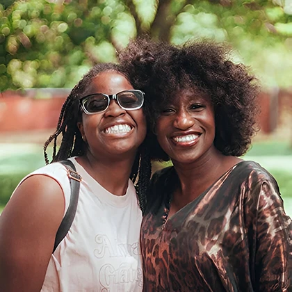 Two women smiling joyfully at the camera, embodying positivity and the beauty of shared moments together.