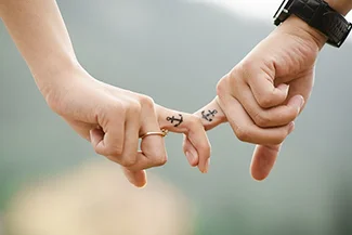 A couple holding hands, showcasing finger tattoos, symbolizing trust as the foundation of their strong relationship.