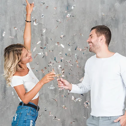 A man and woman toast with champagne glasses, surrounded by colorful confetti, celebrating their achievements together.