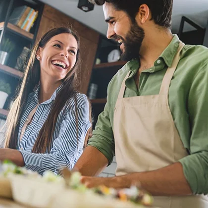 A man and woman smile together while preparing food, showcasing the importance of open communication in their collaboration.