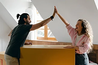 A man and woman joyfully high five in a room, celebrating each other's successes and achievements together.